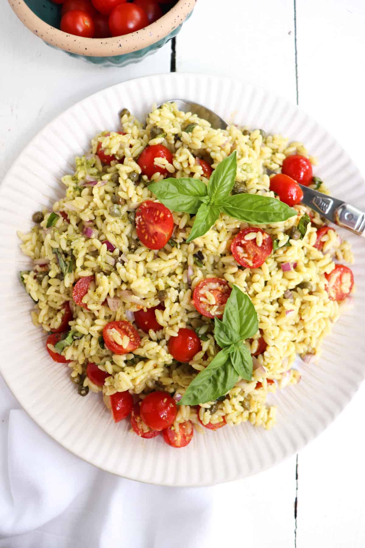 orzo salad on a plate with tomatoes in a bowl above.