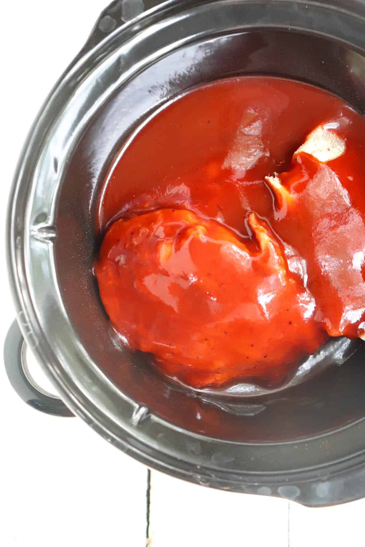 bbq sauce poured over top of chicken in a crock pot.
