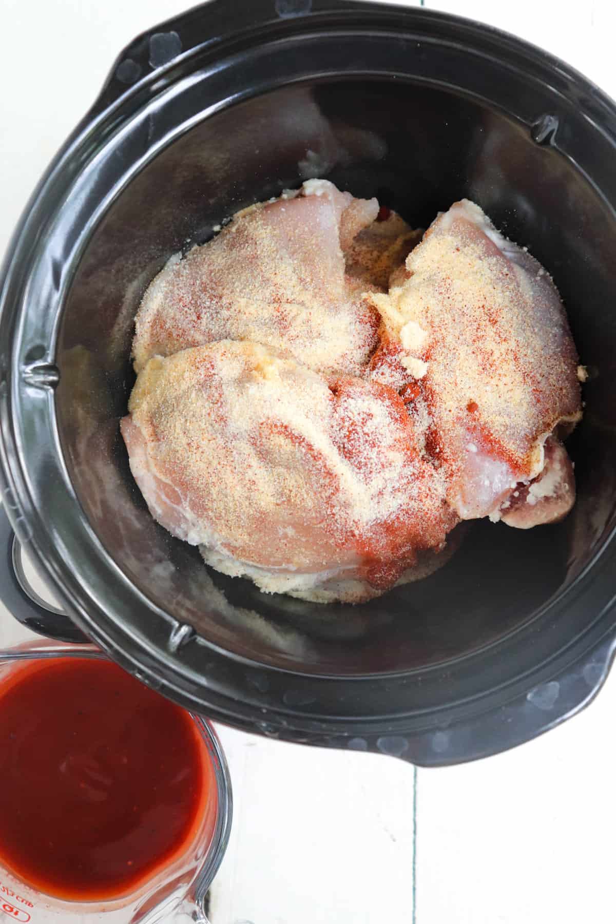 raw chicken thighs in black crock pot with spices sprinkled on top,