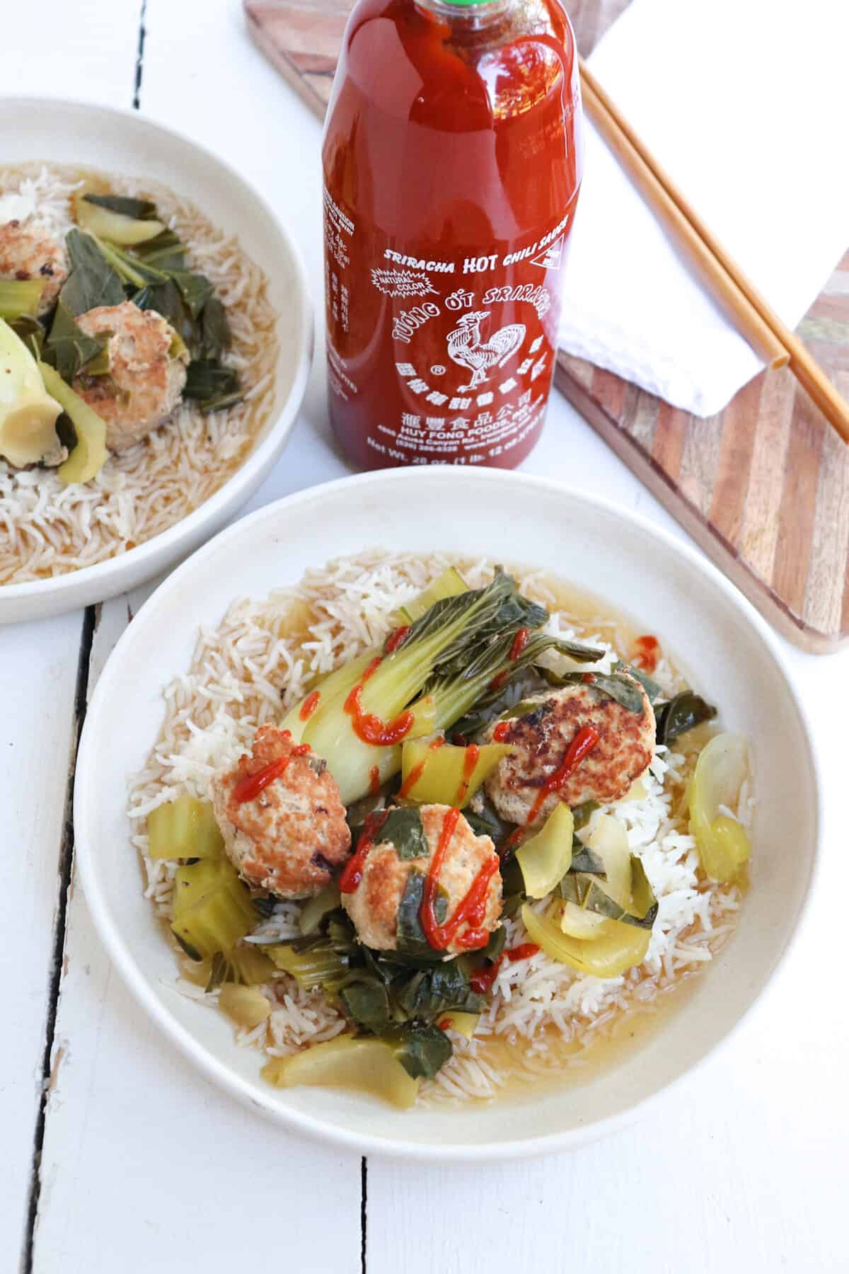 asian pork meatballs with bok choy and rice with sriracha bottle.