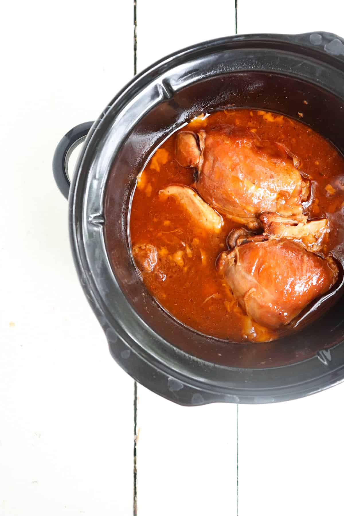 cooked chicken thighs in a black crock pot.