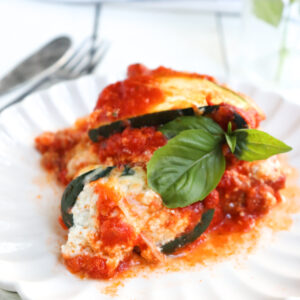 zucchini lasagna roll ups on a white plate garnished with fresh basil.