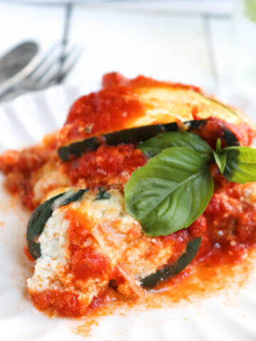zucchini lasagna roll ups on a white plate garnished with fresh basil.