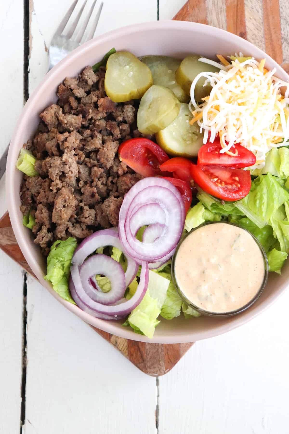 burger salad in a low tan bowl with sauce on the side
