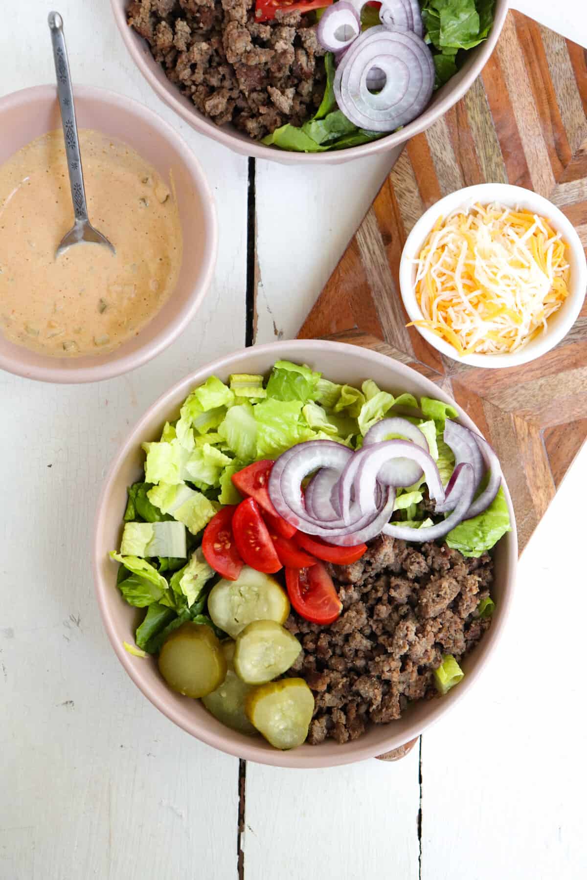 two ground beef burger bowls with sauce and cheese shown on the side.
