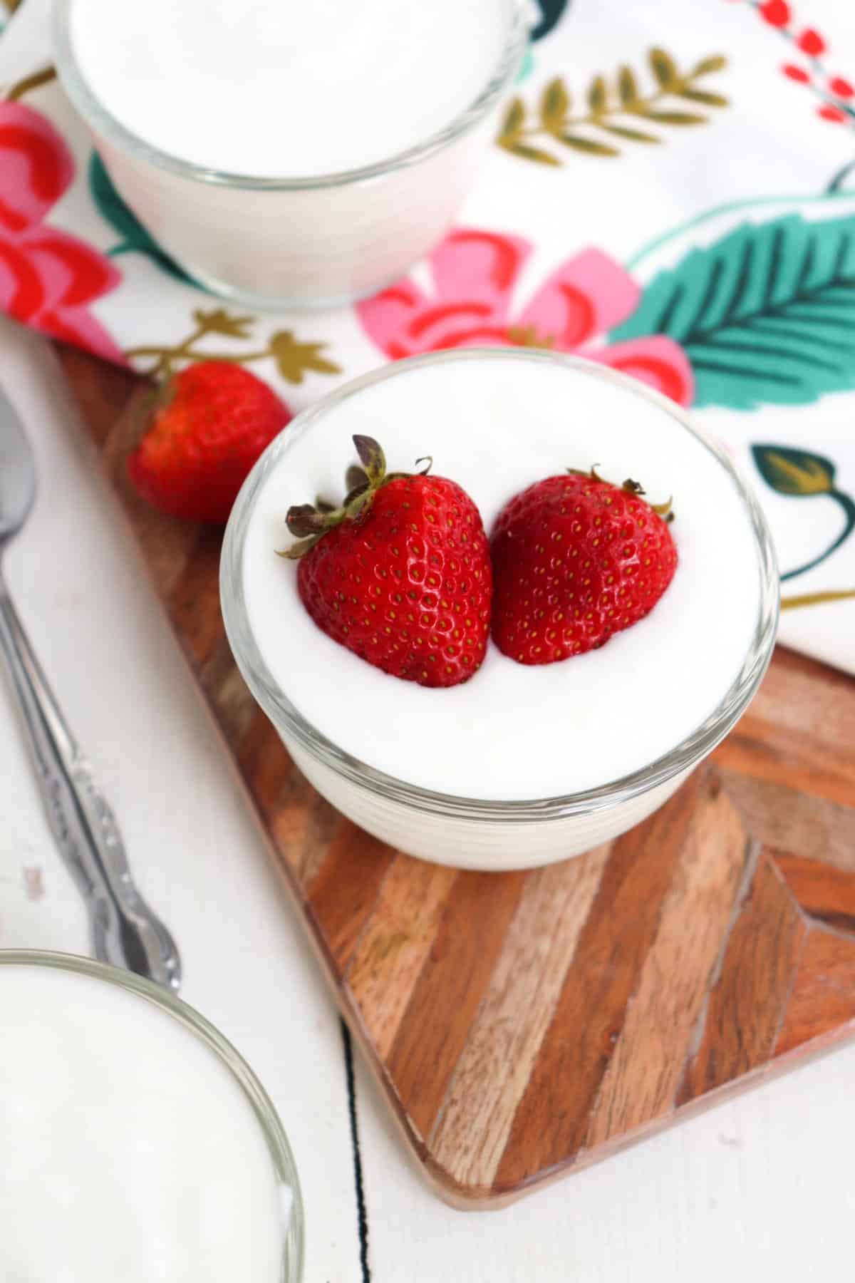 two strawberries on top of a cup of yogurt. 