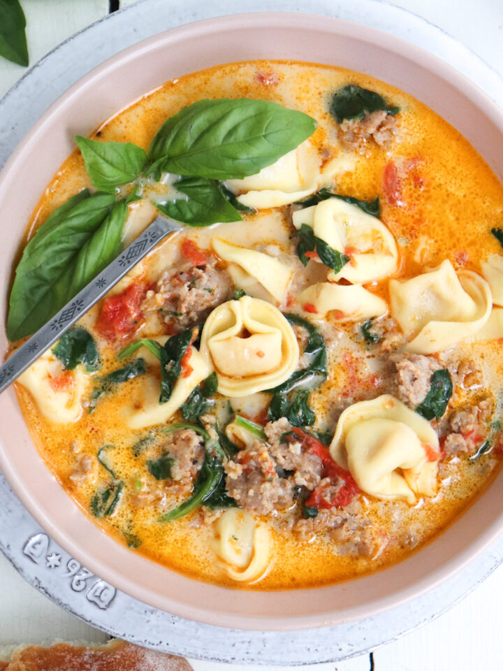 bowl of tortellini soup garnished with basil.