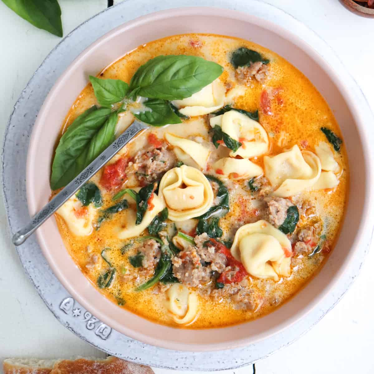 bowl of tortellini soup garnished with basil.