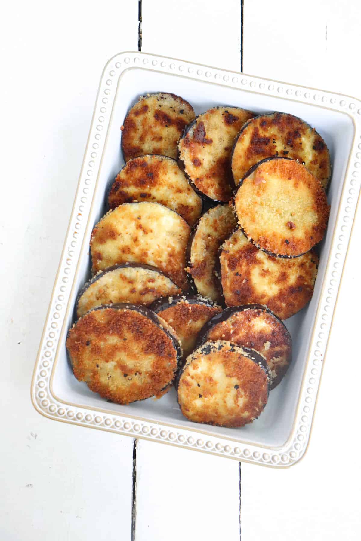 breaded eggplant slices in a white baking dish.
