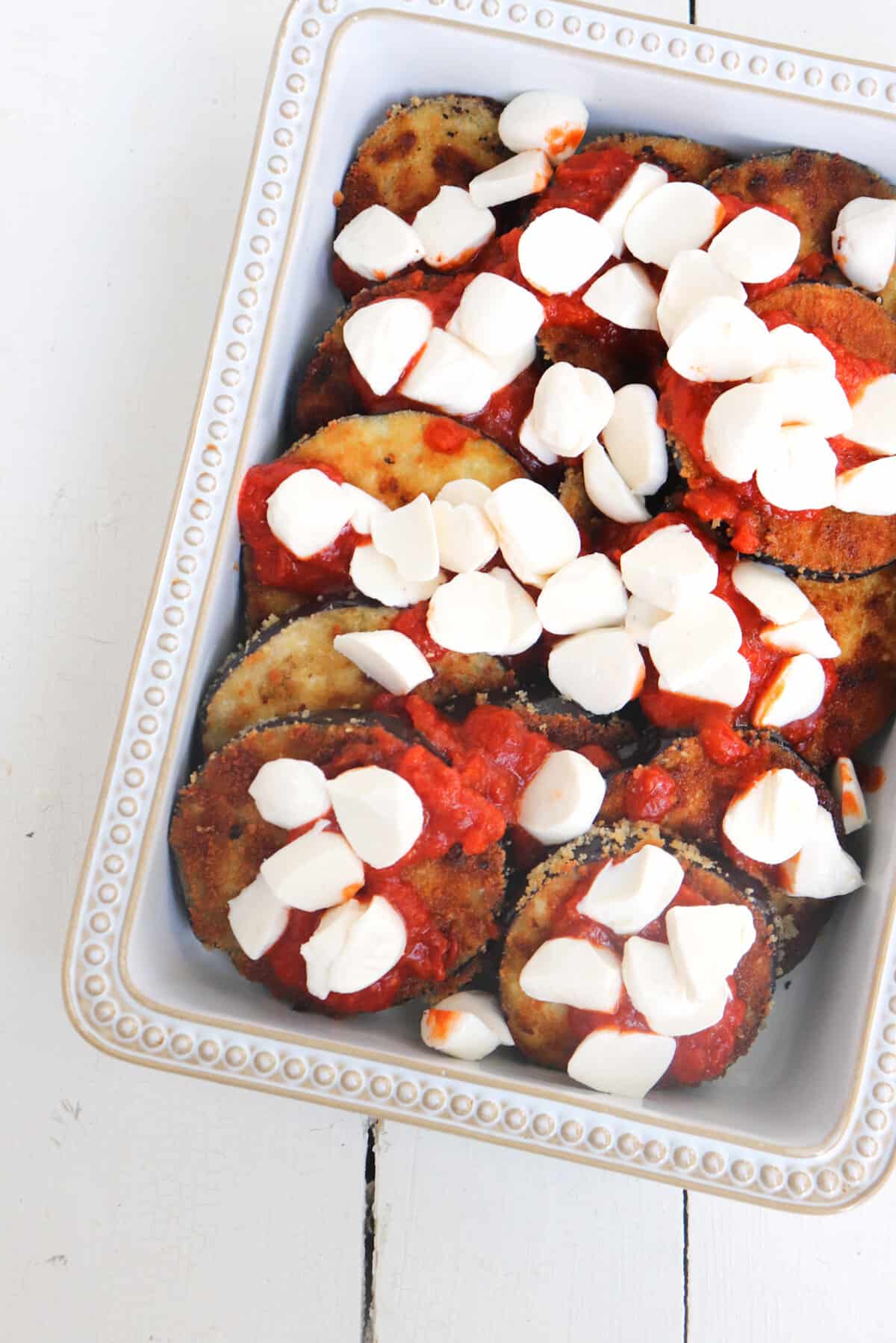 breaded eggplant covered in sauce and fresh mozzarella in a baking dish.
