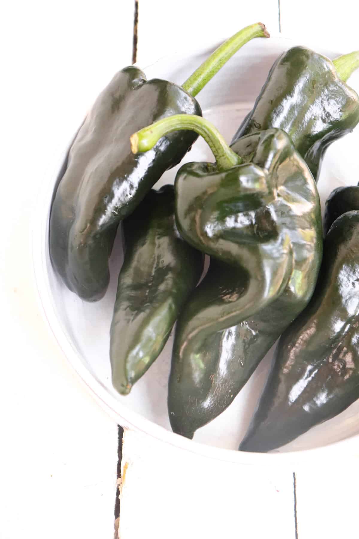 whole poblano peppers in a white bowl.