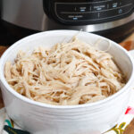 shredded chicken in a white bowl in front of ninja foodi.