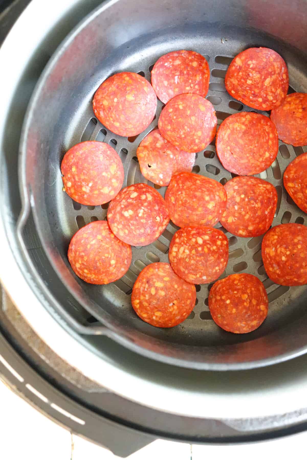 single layer pepperoni slices in air fryer basket.