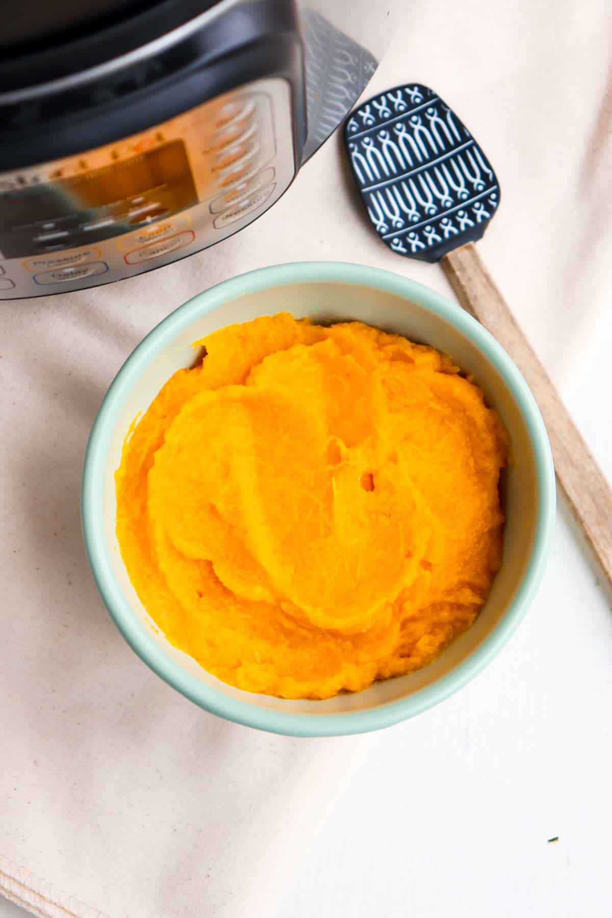 pumpkin puree in a green bowl next to an instant pot. 