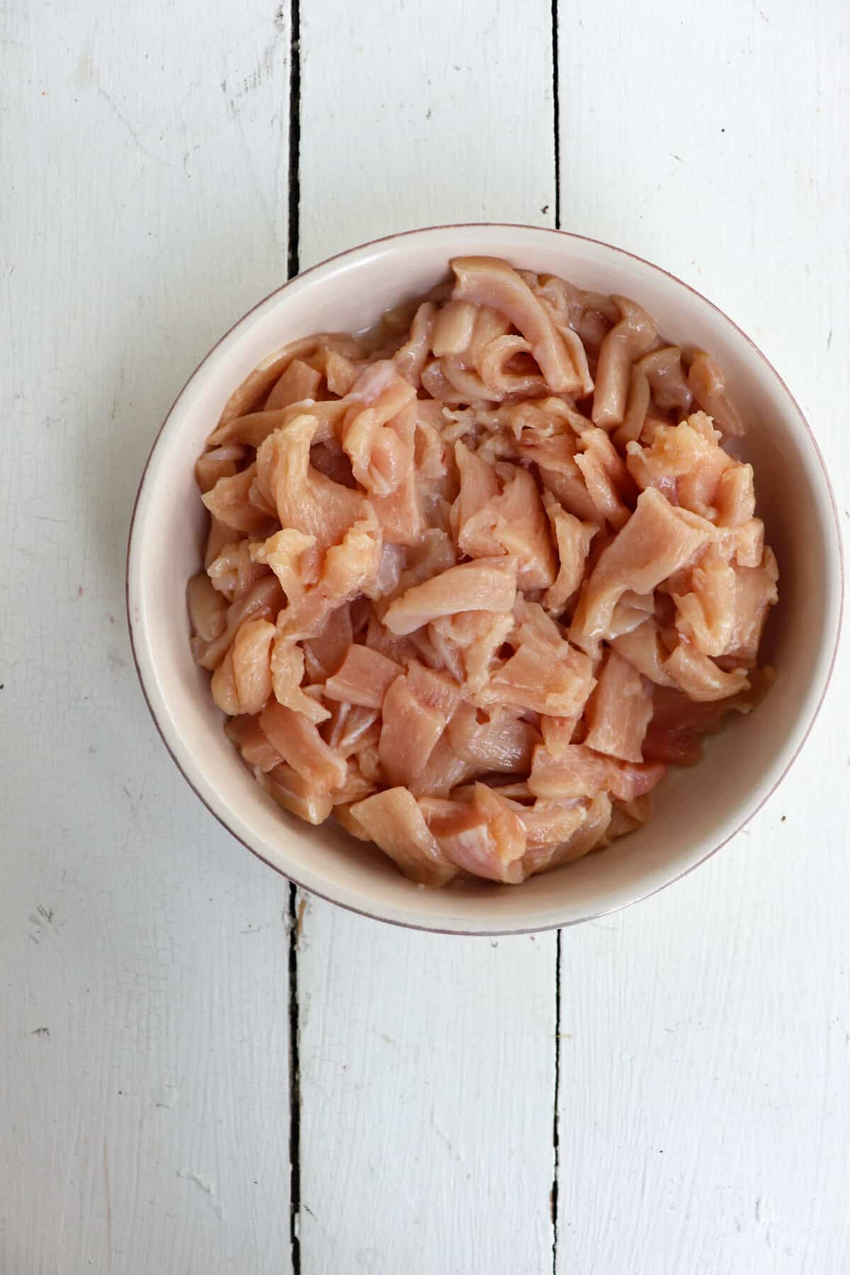 sliced raw chicken in a white bowl.