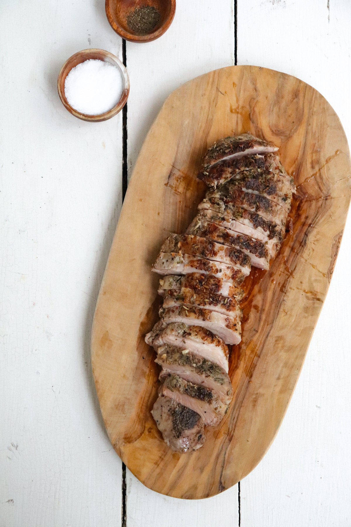 overhead sliced pork tenderloin on a wooden cutting board showing crust.