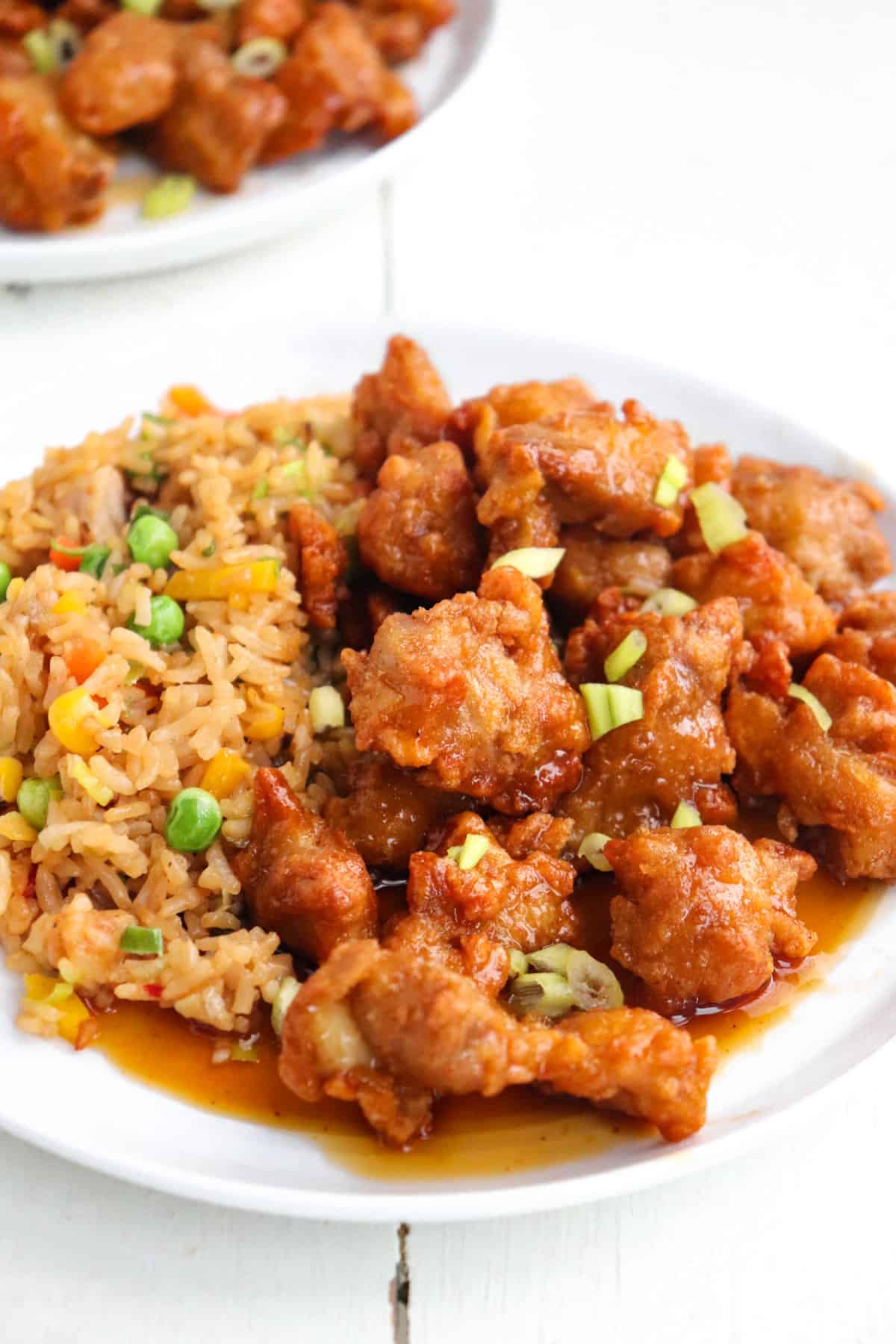plated orange chicken with fried rice and additional chicken in the background.