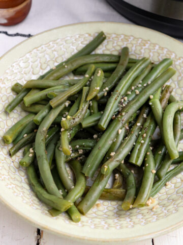 plated seasoned green beans with instant pot in the background.