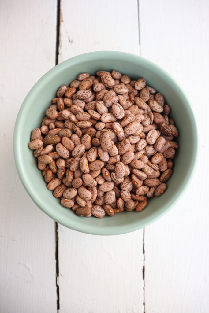 overhead of dry pinto beans in a green bowl.