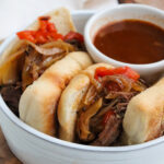 two crockpot venison sandwiches with a small ramekin of au jus.