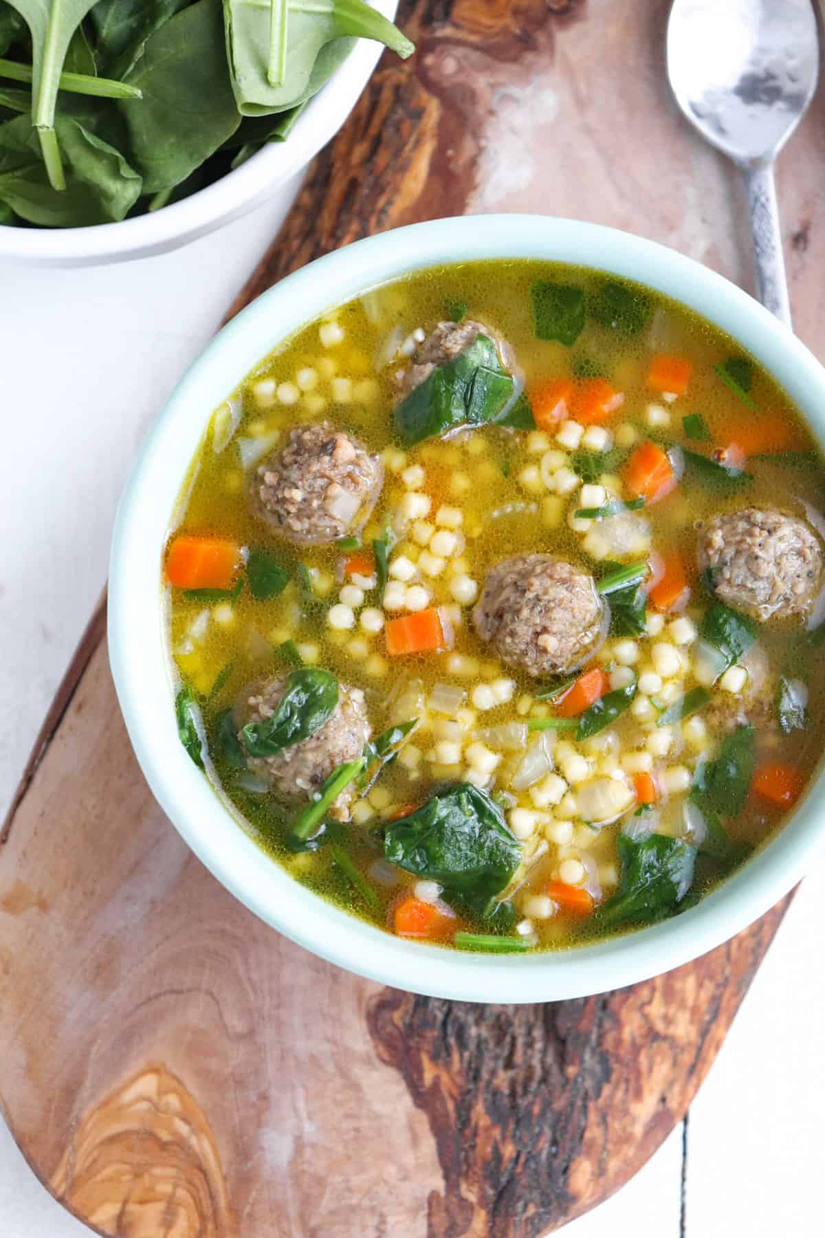 bowl of italian wedding soup with spinach and a spoon on the side. 