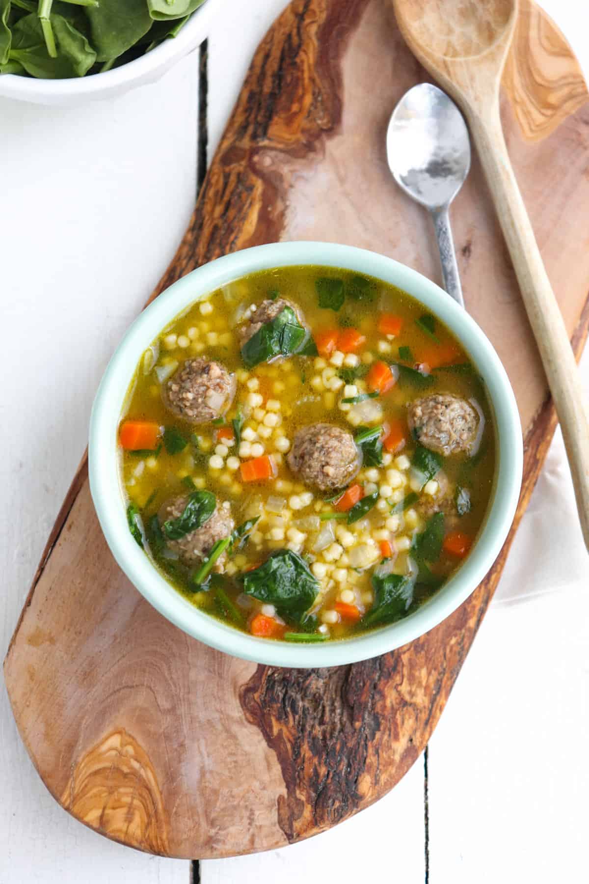 bowl of italian wedding soup with spoons on the side.