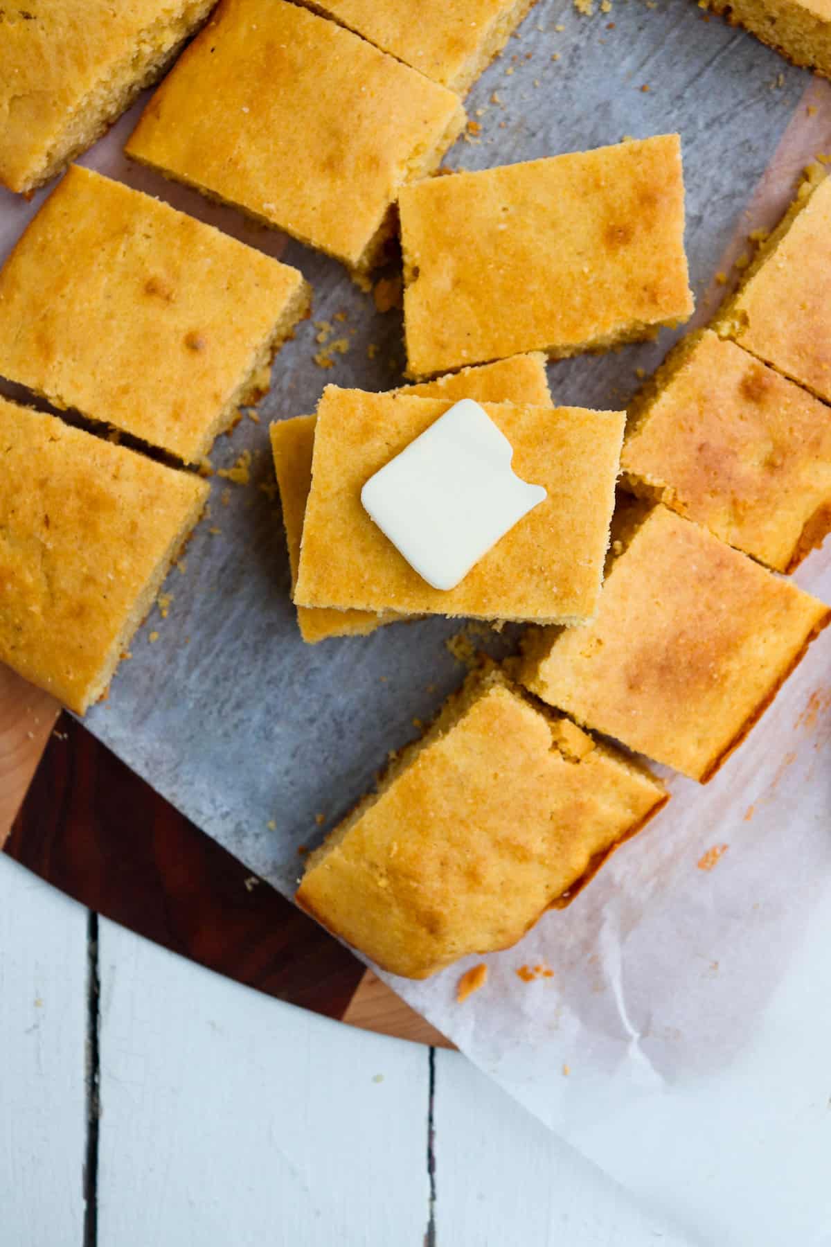 overhead of multiple pieces of cornbread with one having a pat of butter on it.