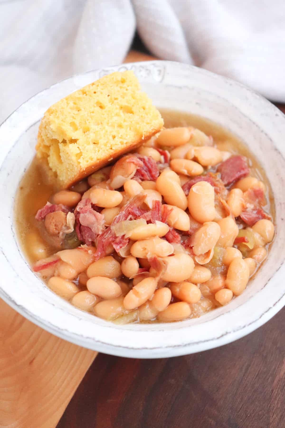 bowl of beans with ham and a slice of cornbread placed in bowl.