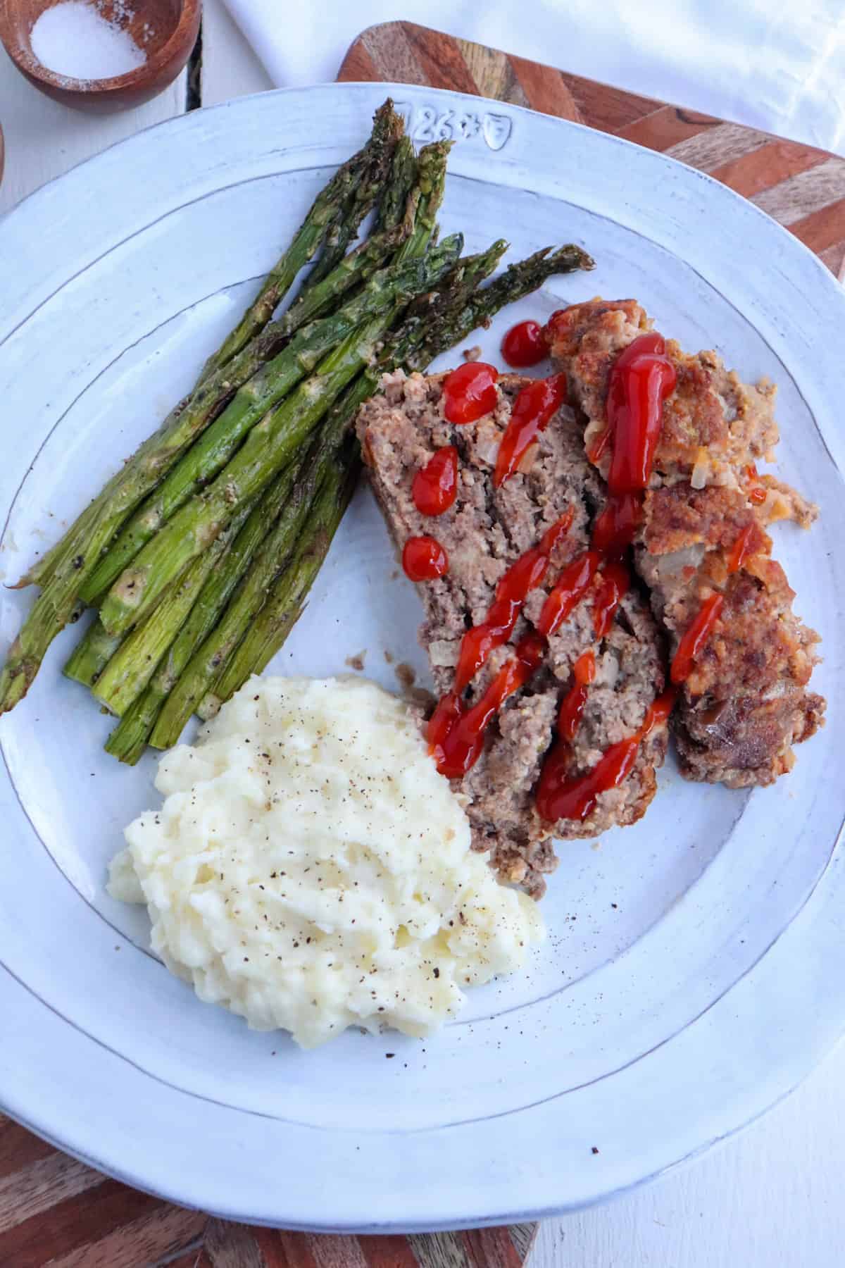 plate of ketchup covered venison meatloaf, mashed potatoes, and asparagus.