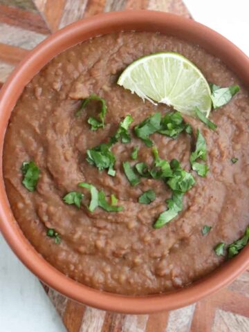 bowl of homemade refried beans garnished with lime and cilantro.