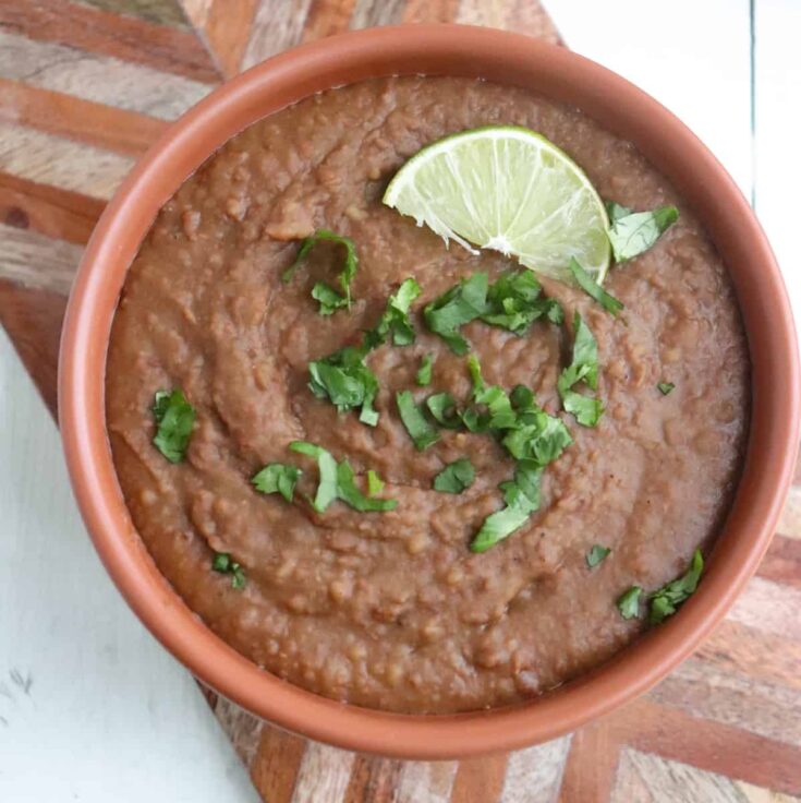 bowl of homemade refried beans garnished with lime and cilantro.