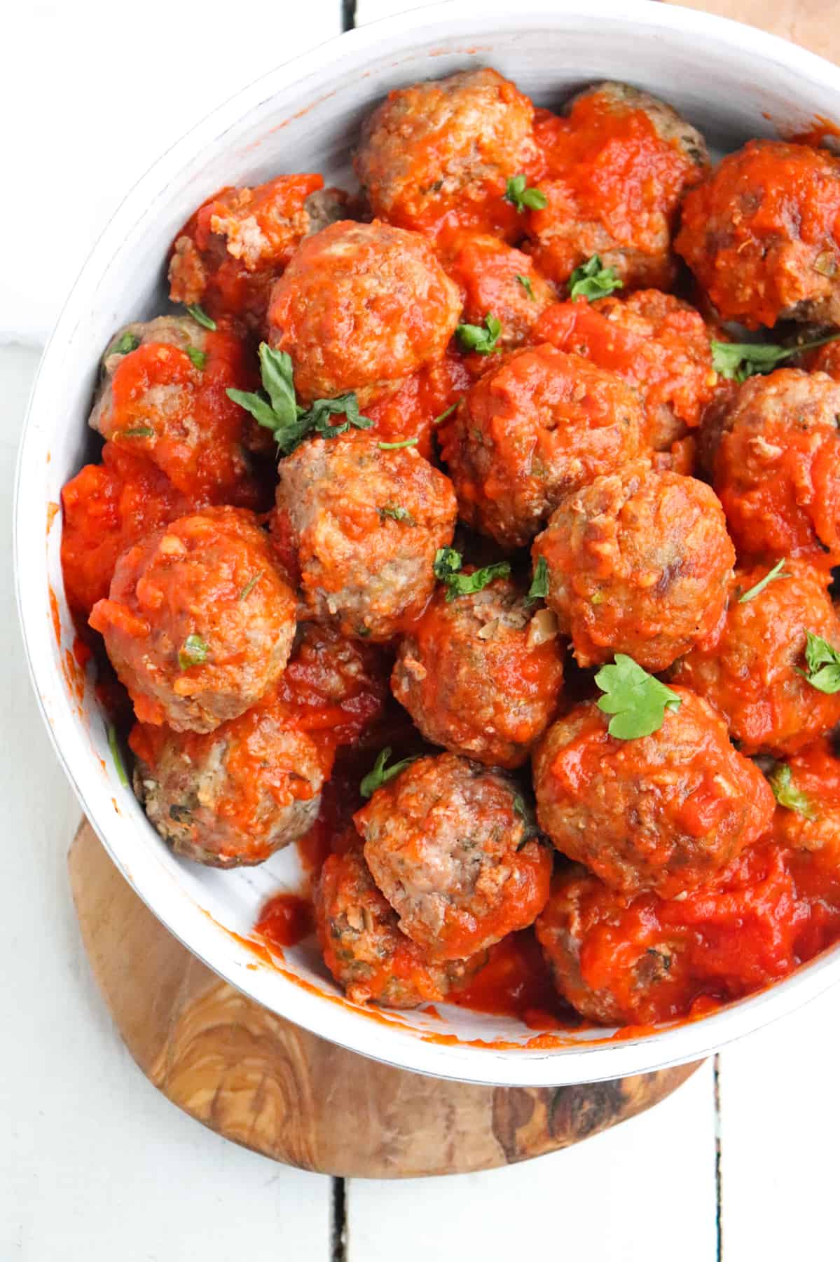 finished meatballs covered in sauce and topped with parsley in a white dish.