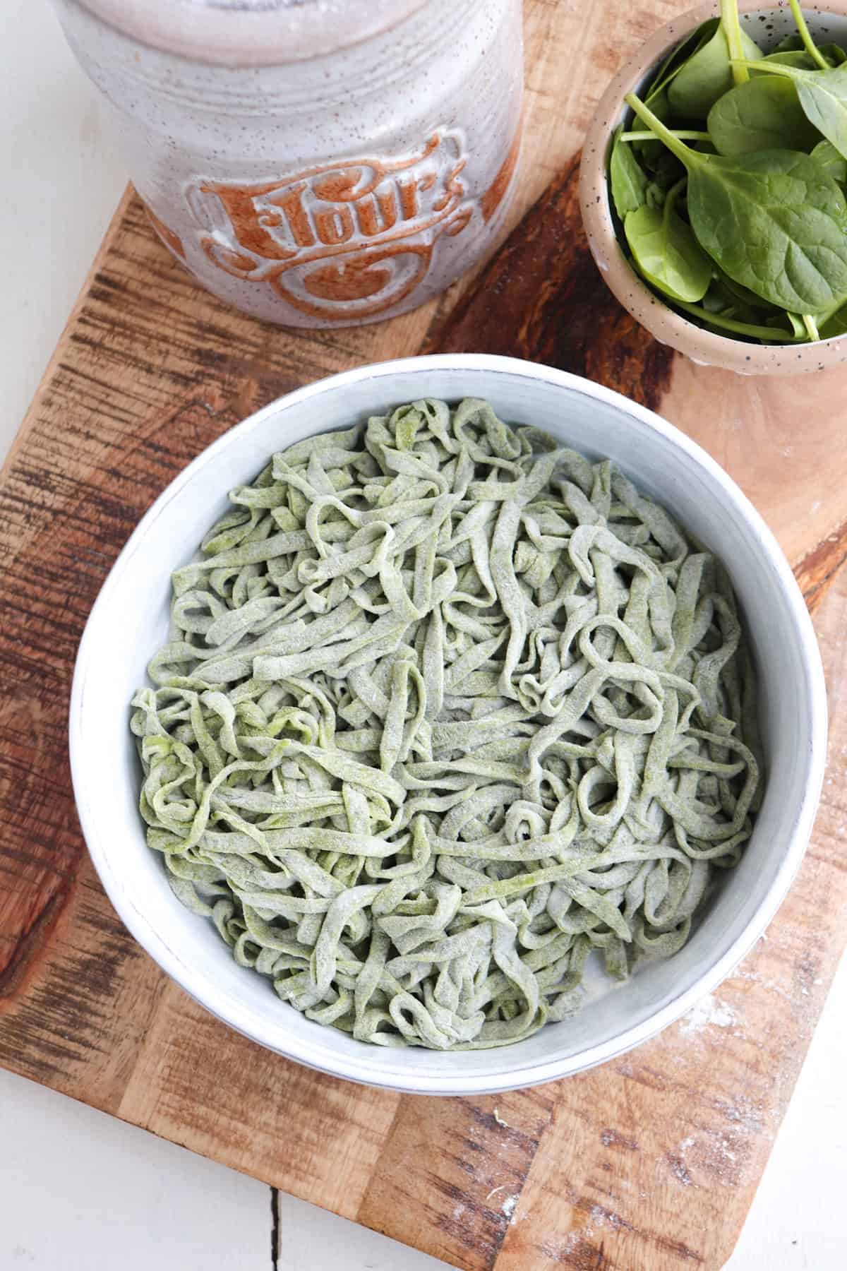spinach noodles heavily flour and shown in a white bowl.