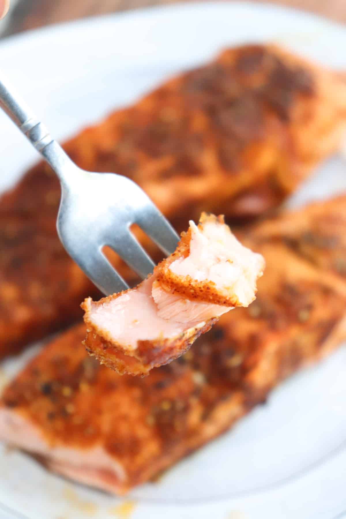 fork holding up bite of salmon in front of fillets.