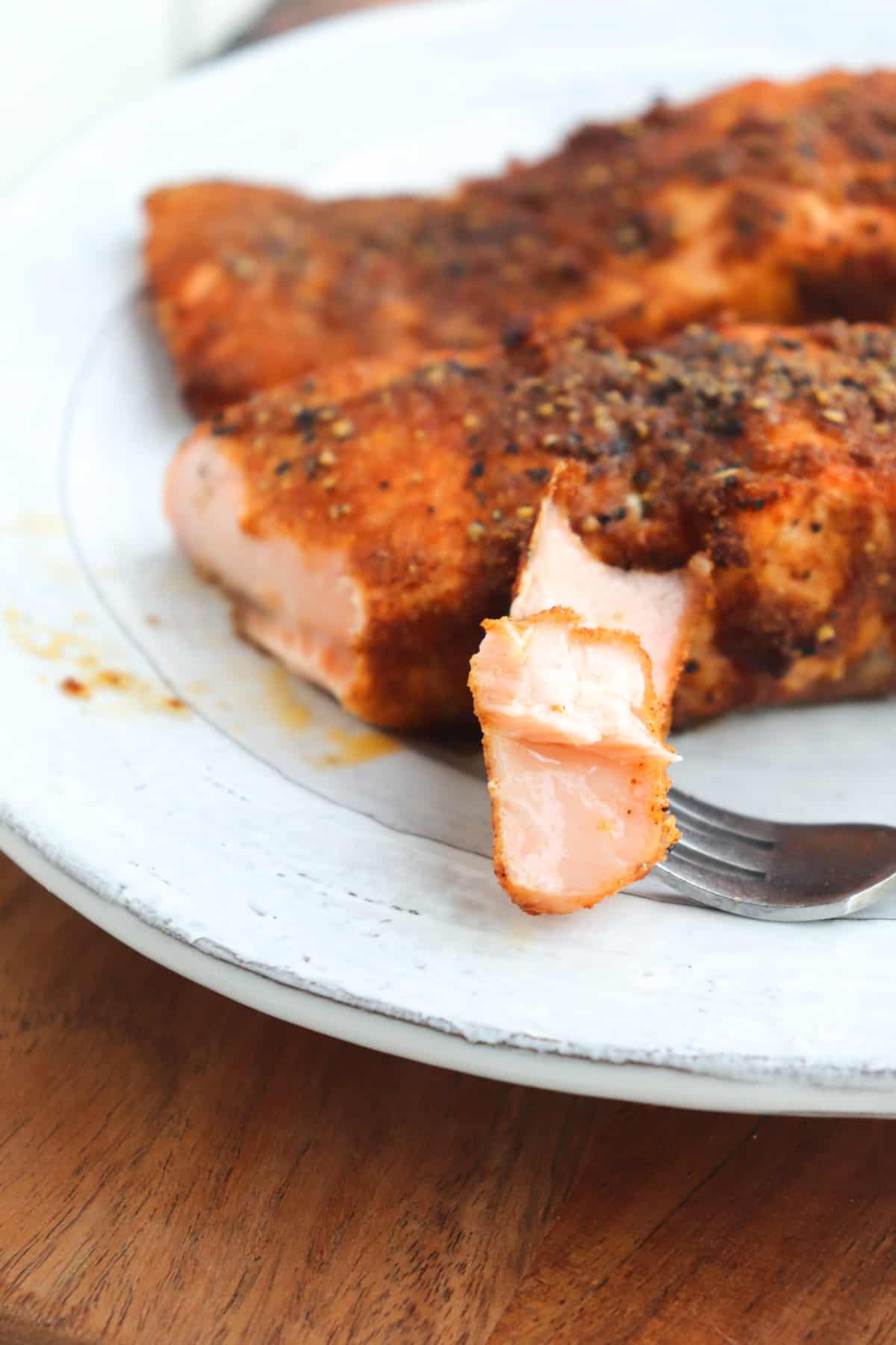 cooked salmon on a plate with a fork holding a bite.