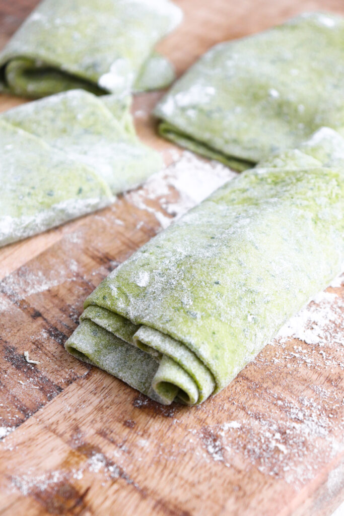 spinach pasta sheets rolled up on a cutting board.