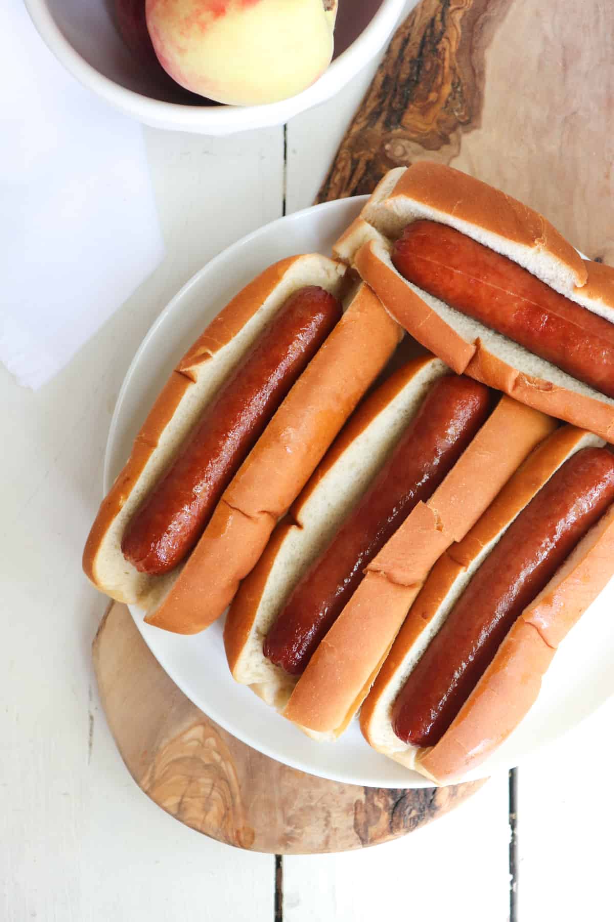 four air fried hot dogs on a white plate with peaches to the side.
