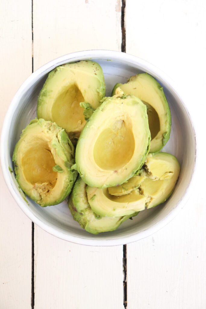white bowl filled with avocado halves.
