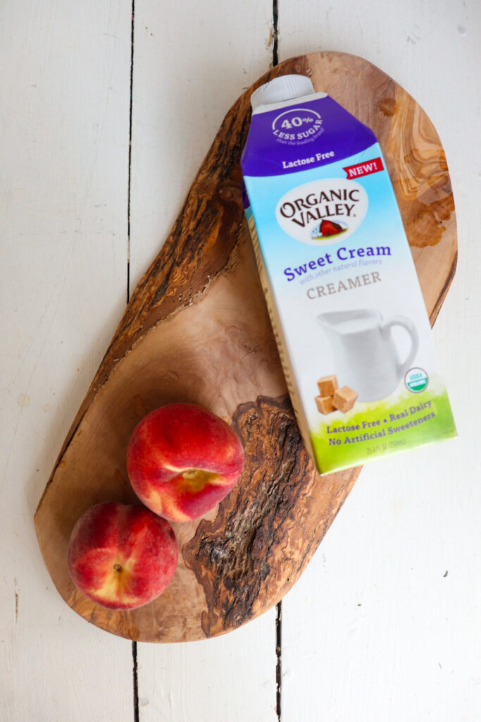2 peaches and sweet cream creamer on a wooden board.