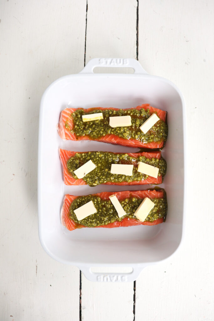 3 salmon filets with pesto and butter on top.