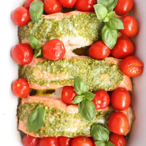 cropped finished pesto butter salmon with tomatoes garnished with basil.