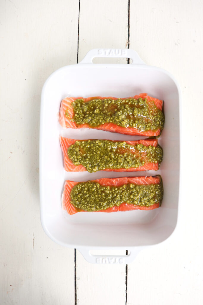 3 salmon filets topped with pesto in a white dish.
