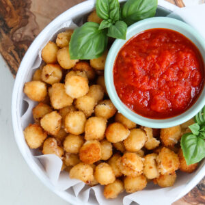 a plate of fried mozzarella balls that features a side of marinara and fresh basil.