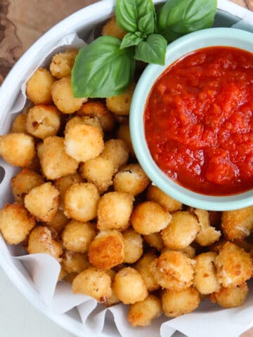a plate of fried mozzarella balls that features a side of marinara and fresh basil.