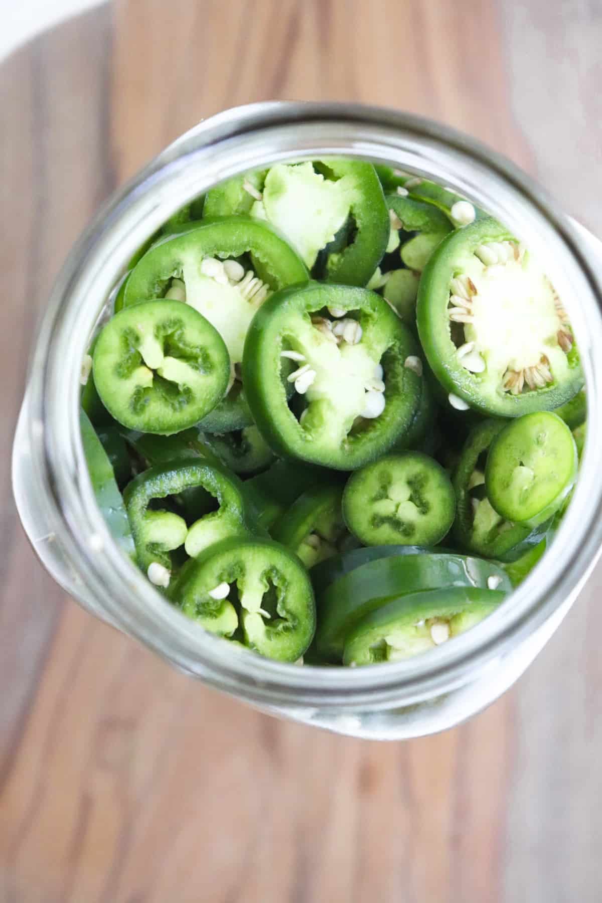 slices of fresh jalapeno in a large mason jar.