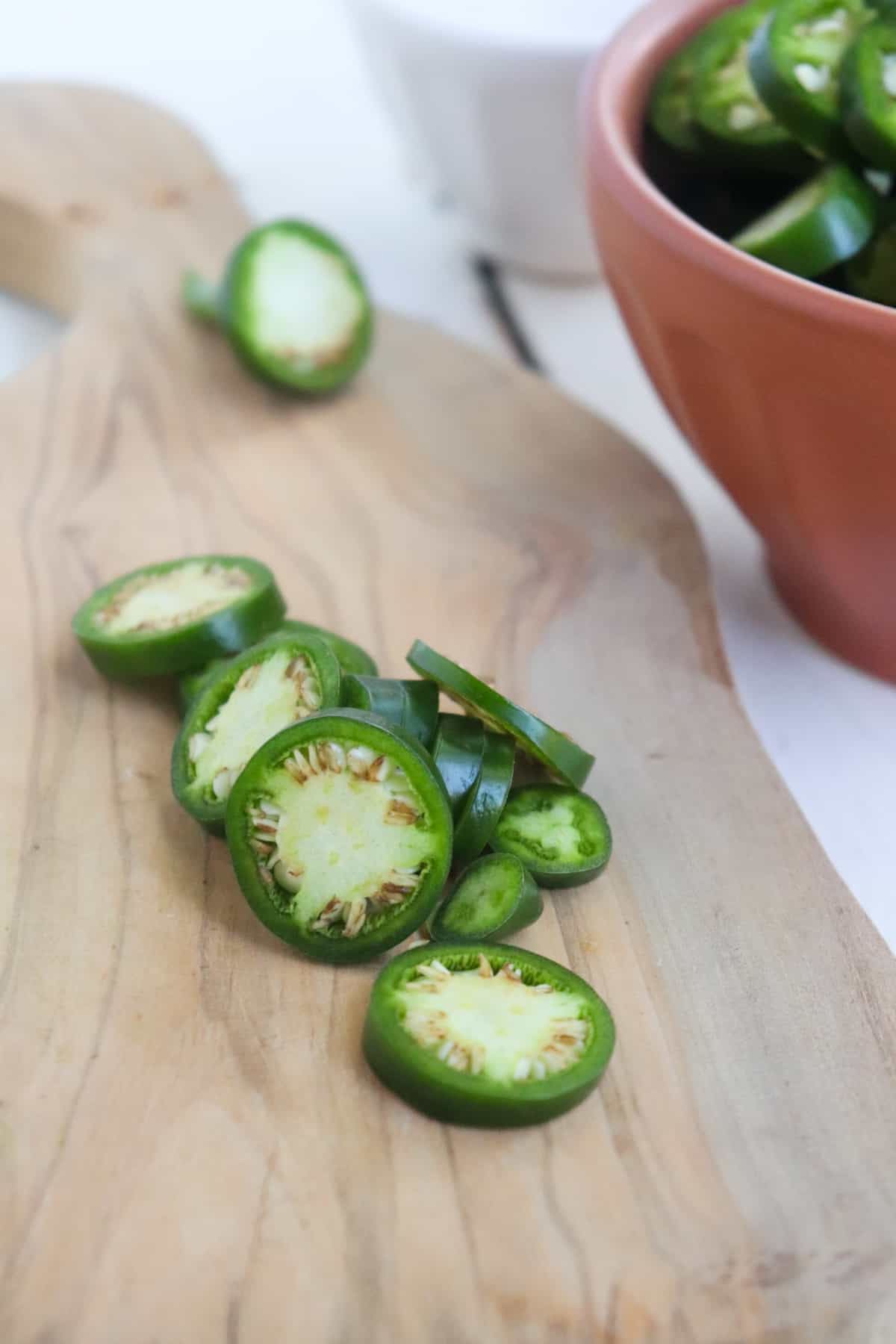slices of fresh jalapeno on a wooden cutting board.