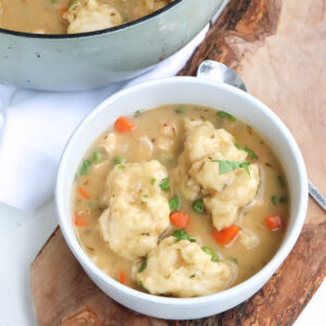 chicken and dumplings in a bowl with dutch oven in the background.
