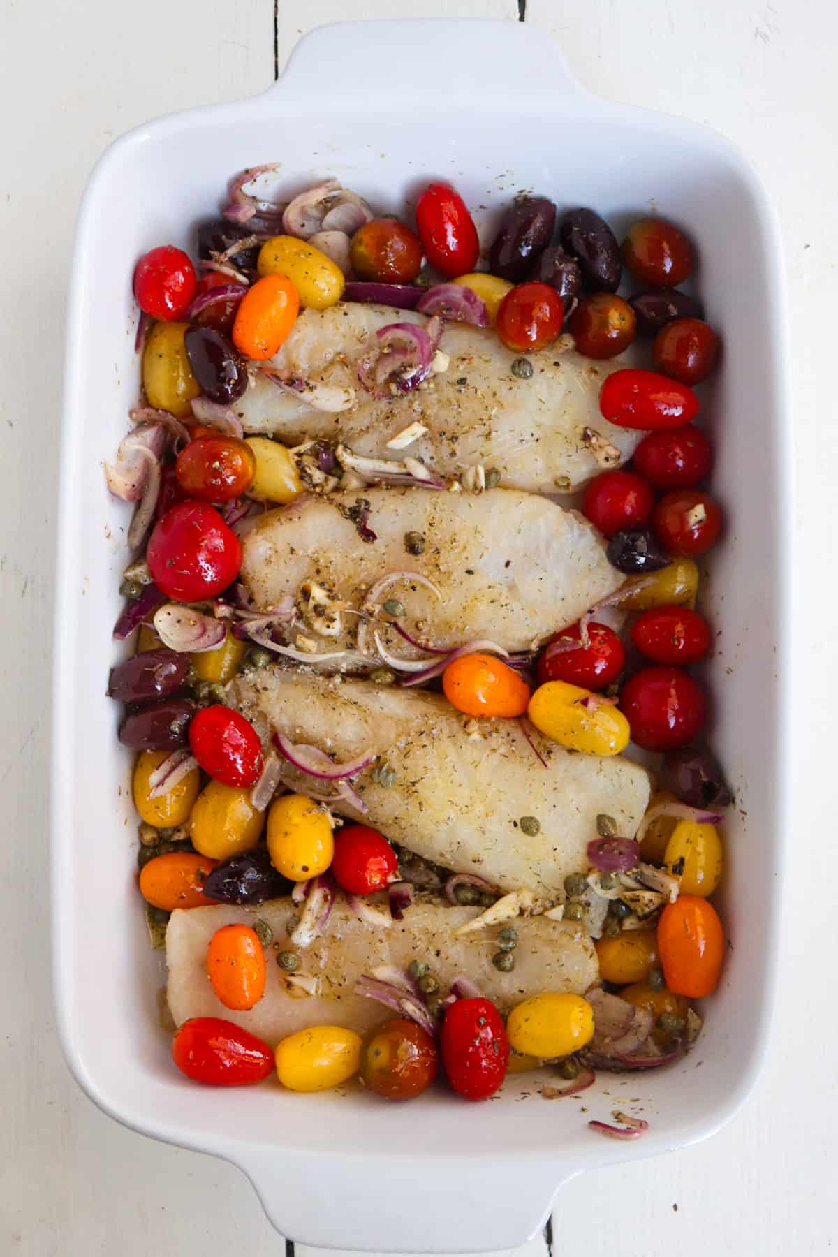 cod pieces added to a white dish of baked tomatoes.