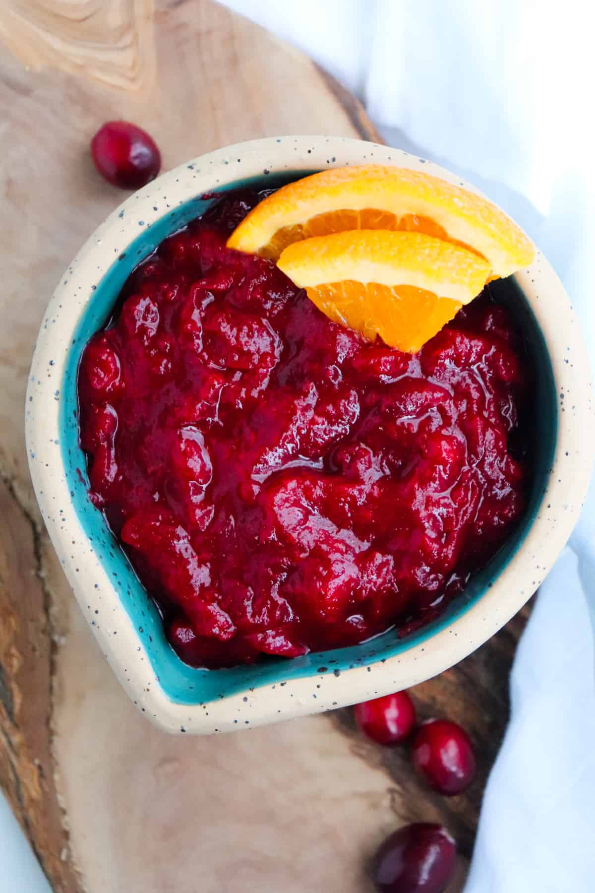 overhead shot of finished cranberry orange sauce in a green bowl with orange slices for garnish with cranberries scattered around.