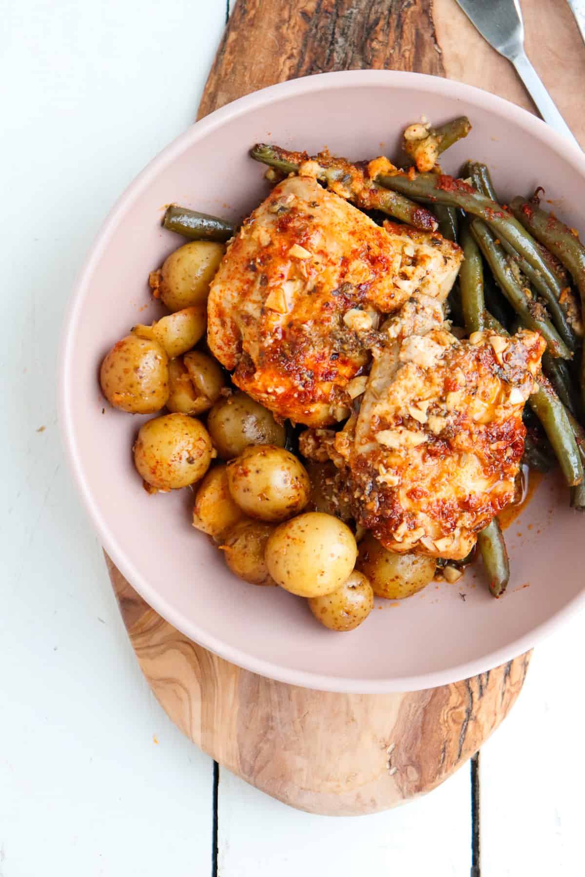 finished dish of potatoes, green beans, and two chicken thighs on top in a pink low bowl.